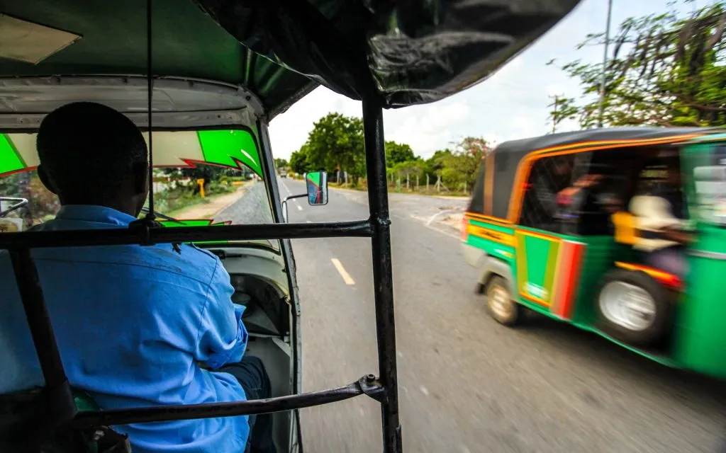 Vista do banco do passageiro quando se conduz um tuk tuk (riquexó de três rodas) com outro que vem na direção oposta, do outro lado da estrada. Malindi, Quénia
